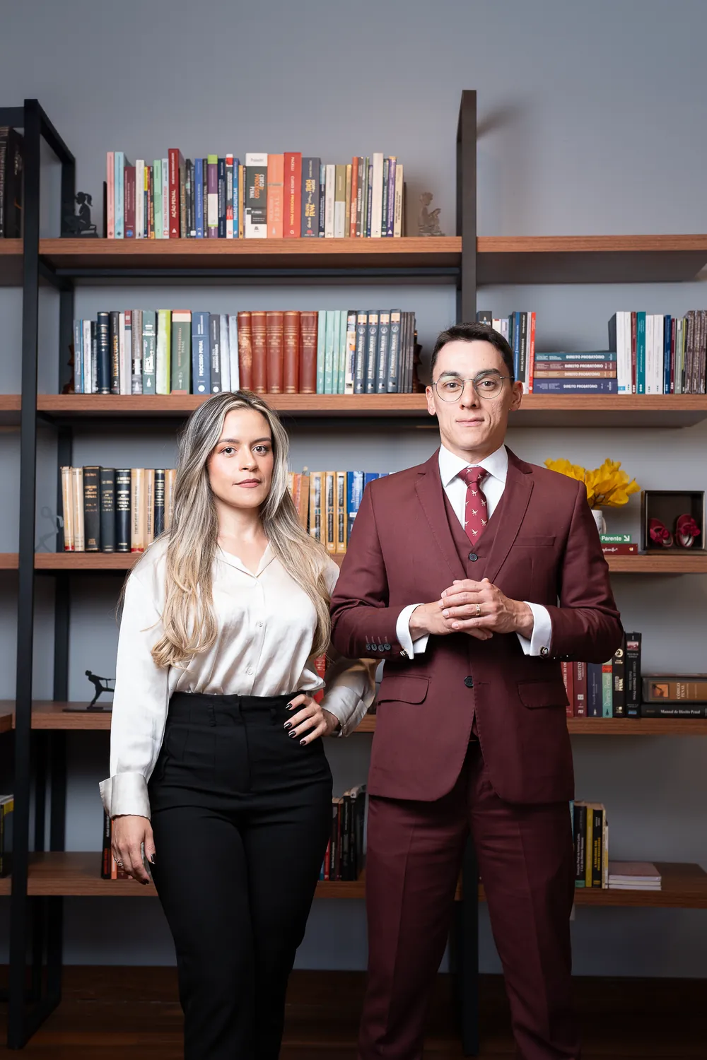 Dois integrantes da equipe diante da estante de livros